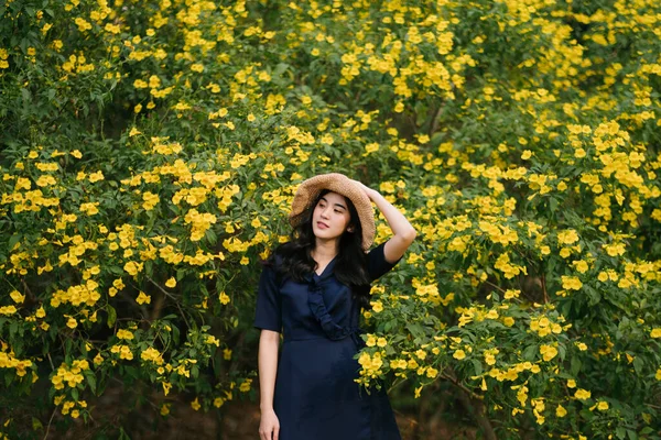 可愛いですタイの女の子立っています前のために多くの黄色の花タッチ彼女の帽子 — ストック写真