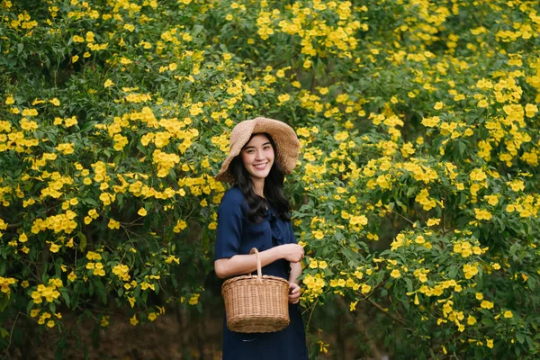 黄色の花のバスケットを保持し 美しい笑顔でカメラを見ての間でタイの女の子の側 — ストック写真