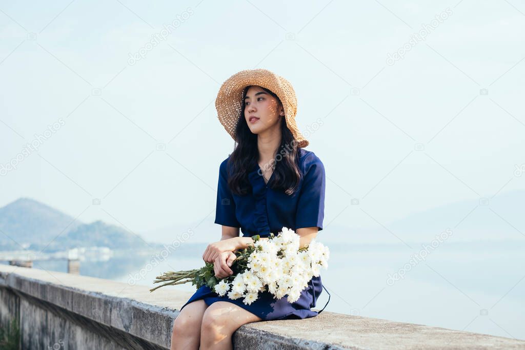 A lovely Thai girl sitting at the dam holding the white flowers in her arms.