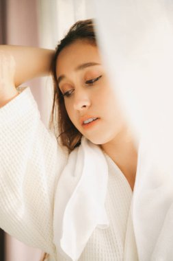 Beyaz perdenin arkasında beyaz bornozlu seksi genç bir kadın var. Boşluğu kopyala.