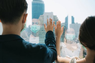 Arka plan - doktor maskesi takan Asyalı çift cam pencereye dokunarak şehir manzarası gökdelenine bakıyor. Covid19 krizi sırasında insanlar evde kalıyor. Karantina.