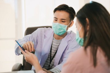 Asyalı Taylandlı doktor maske takıyor ya da hastanede ya da klinikte hasta kadınla konuşuyor. Sağlık hizmetleri teşhisi. 