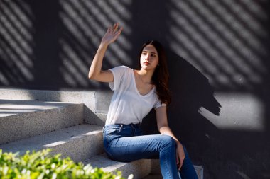 Taylandlı kadın merdivenlerde oturuyor, yüzünde güneş ışığı var..