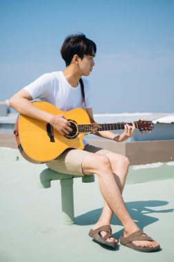 Güneş ışığında çatıda gitar çalan adam..