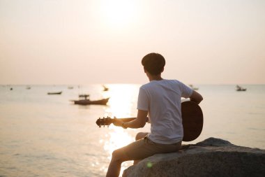 Gün batımında plajda gitar çalan adam..