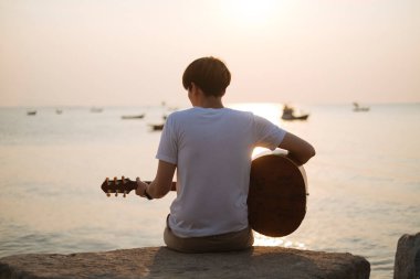 Gün batımının güzel plajında oturan ve gitar çalan bir adam..