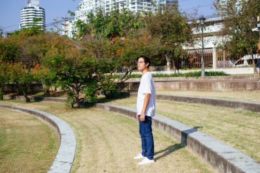 Şehir parkında çimlerin üzerinde duran Taylandlı adam..