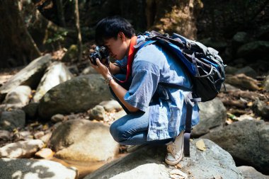 Ormandaki bir kayanın üzerinde oturup fotoğraf çeken bir adam..