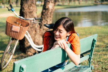 Güneş ışığında yeşil bir bankta oturan tatlı bir kız. Arka planda bisiklet var..