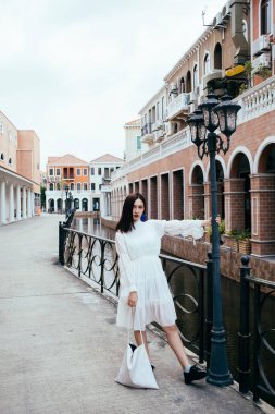 Beyaz elbiseli güzel bir kadın sokak lambasını tutuyor..