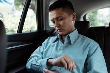 Bir iş adamı arabada otururken sağ kolunun düğmesini ilikliyor..