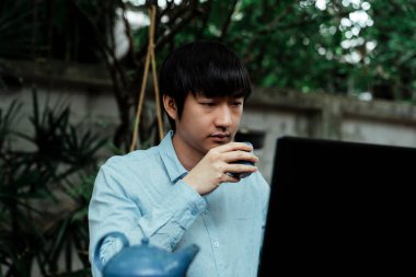 Parkta çaydanlığıyla çalışan mavi gömlekli bir adam..