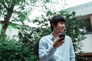 Kafe bahçesinde dikilirken telefonunu tutan bulanık tişörtlü bir adam..