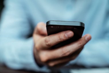 Mavi tişörtlü serbest çalışan bir adamın elinde akıllı bir telefonun yakın çekimi..