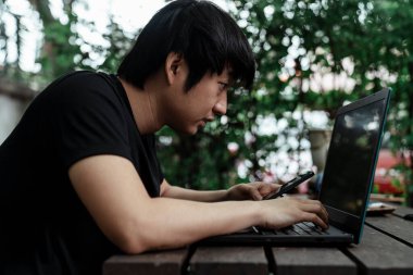 Siyah tişörtlü bir adam akıllı telefonu ve bilgisayarı arasındaki bilgiyi tekrar kontrol ediyor..