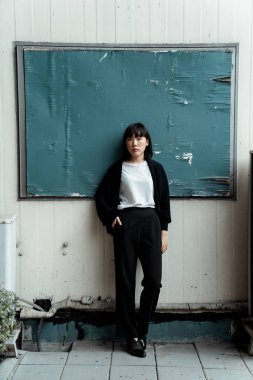 Siyah beyaz elbiseli kız beyaz duvardaki tahtanın önünde duruyor..