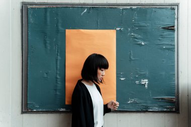 Siyah beyaz kumaşlı kadın turuncu kağıtla tutturulmuş tahtada duruyor..