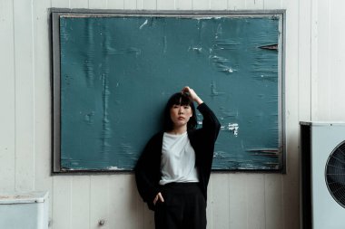 Siyah beyaz giysili bir kadın tahtada dikilirken kafasına dokunuyor..