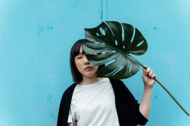 Elinde büyük bir yaprakla mavi arka planda duran bir kadın..