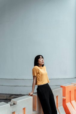 Turuncu ve siyah kadın beyaz duvarın önünde oturmuş gökyüzüne bakıyor..