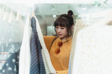 Sarı kazak giyen tatlı kız mağazada kadın kıyafetleri arıyor..