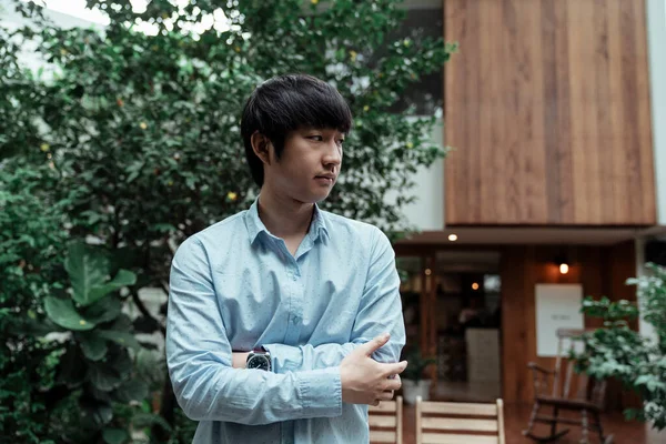 A cool standing posture of a freelance guy infront of the wooden cafe and garden.