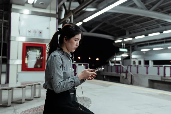 Thai officer woman with ponytail hair sitting at the skytrain\'s station and get into her world with the music from her phone.
