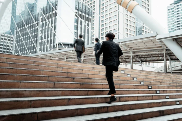 Behind the businessman who walking up the stair at the public square in the city.