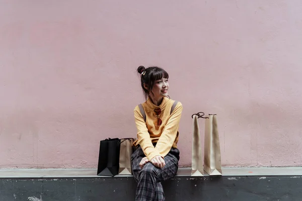 Nettes Mädchen Mit Gelbem Pullover Sitzt Mit Papiertüten Auf Rosa — Stockfoto
