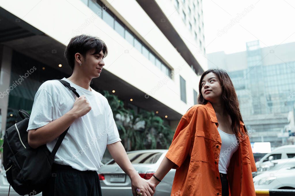 Teenage couple walking along the street with holding hands, a guy looking at his girl with love, a girl looking back at her boy.