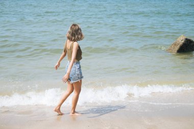 Sahilde yürüyen seksi kız deniz dalgalarına bakıyor..