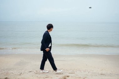 Kumsalda yürürken uçan kuşa bakan iş adamı..