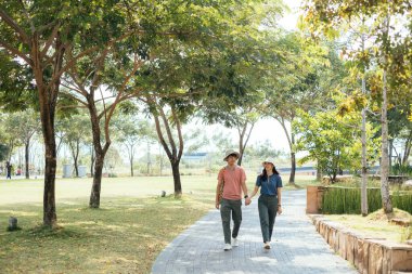 Parkta yürüyen şapka takan Asyalı çift..