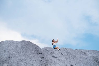 Mavi gökyüzünün altındaki bir kaya tepesinde oturan tatlı kız..