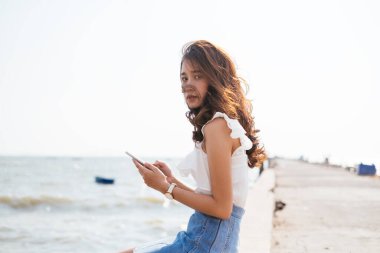 Asyalı uzun saçlı, rüzgarlı bir günde rıhtımda telefon kullanıyor..