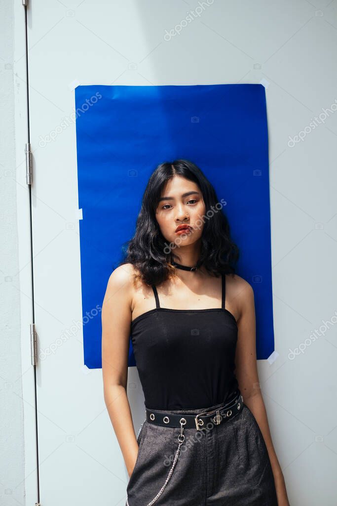 Fabulous girl infront of white wall with blue paper, looking at the camera.