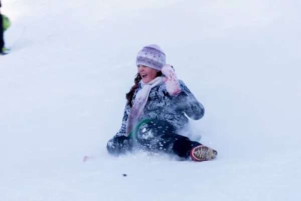 Meisje in de winterkleren is rijden op een dia sneeuw. — Stockfoto