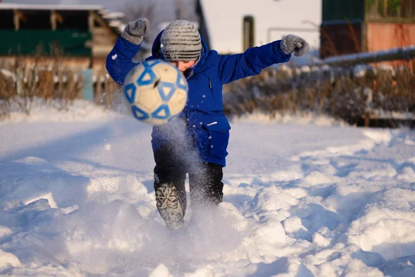 Schoolboy boy kicks the ball playing in winter football on the s Stock Picture