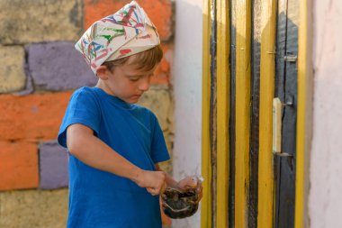 Bir çocuk kapıyı açık hava yaz aylarında açık havada boyama tarafından bir resim yapar. Düzeni tekrar kurmak ve binanın görünümünü iyileştirmek. Fırça boya kavanoza dips.