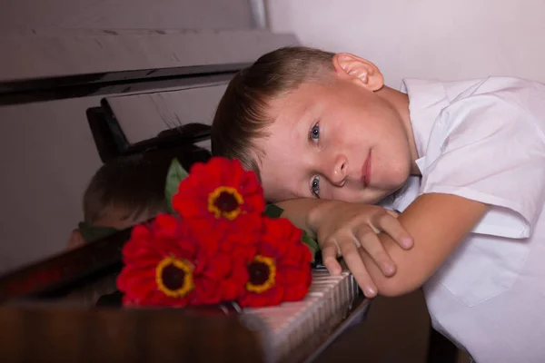 Ένας νεαρός πιανίστας άνδρας κάθεται πίσω από ένα πιάνο με ένα μπουκέτο λουλουδιών — Φωτογραφία Αρχείου