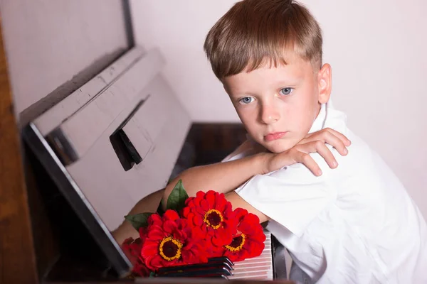 一个年轻的钢琴家坐在钢琴后面, 捧着一束花 — 图库照片