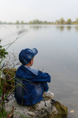 Nehir kıyısında çocuğa yayılıyor. Büyük kayanın bould üzerinde oturuyor