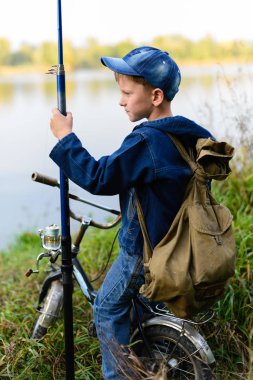 Elinde bir olta ile nehir kıyısında bir balıkçı çocuk