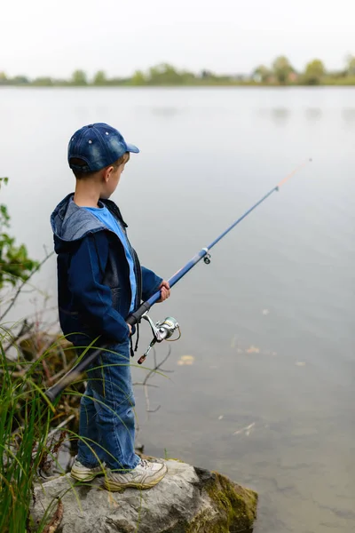 Un ragazzo pescatore sulla riva del fiume con una canna da pesca in mano — Foto Stock