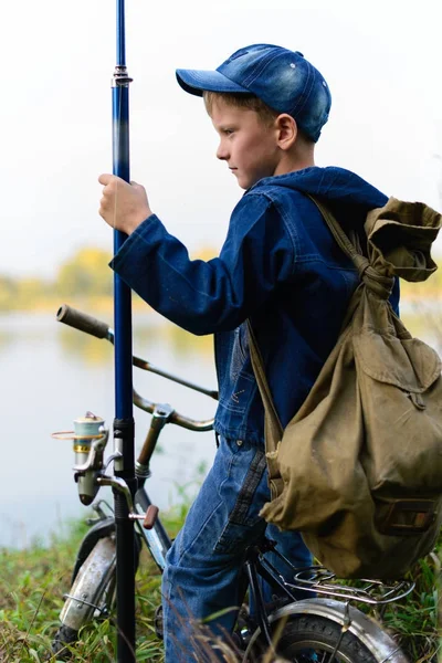 Un ragazzo pescatore sulla riva del fiume con una canna da pesca in mano — Foto Stock