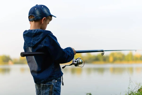 Un ragazzo pescatore sulla riva del fiume con una canna da pesca in mano — Foto Stock