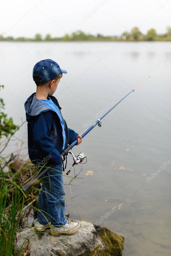 A fisherman boy on the river bank with a fishing rod in his hand