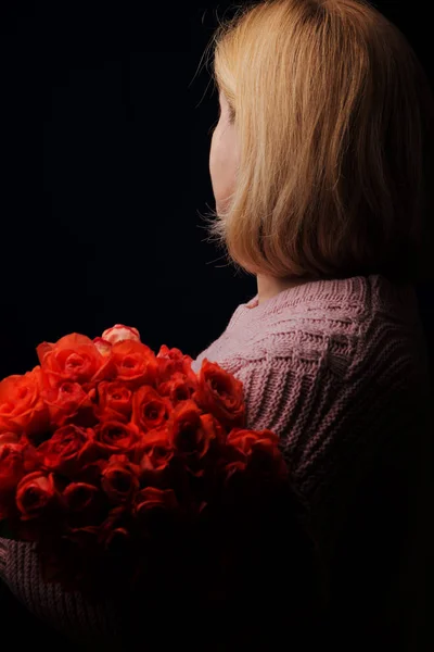 La donna tiene un mazzo di rose arancioni. Si allontanò dallo spettatore. Studio foto su uno sfondo scuro . — Foto Stock