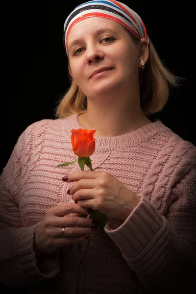 Žena v šátku s červenou růží v ruce na černé látce. Natáčení ve studiu. — Stock fotografie