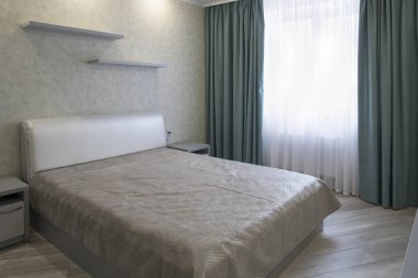 Rahat yatak odası iç tasarımı, beyaz modern yatak, gri duvarlar ve zemin, mavi perdeler.